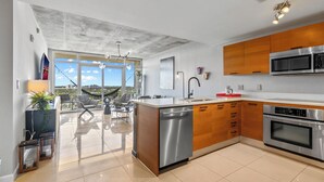 Une cuisine moderne dotée d’appareils électroménagers en acier inoxydable, de meubles en bois et d’une grande fenêtre offrant une vue sur le paysage urbain.