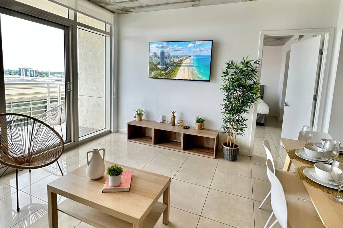 A modern living room with a large TV, a dining area, and a balcony with a view.
