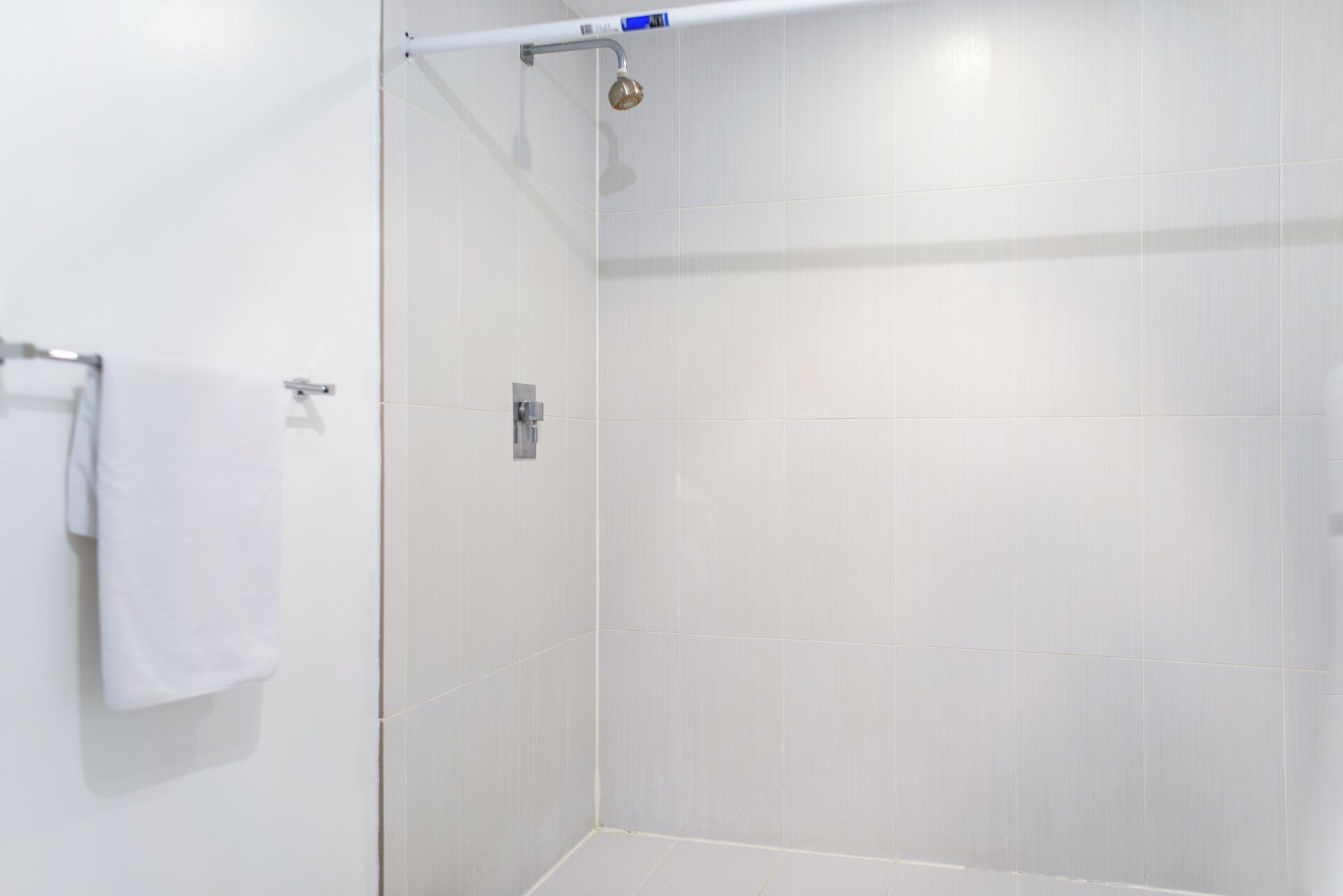 A white tiled shower with a towel rack and a showerhead.