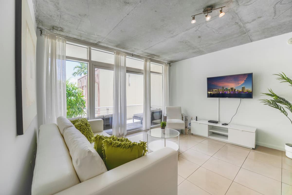 A modern living room with a white sofa, a glass coffee table, and a flat-screen TV mounted on the wall.