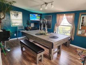 Un comedor con una mesa de madera, una banca y un televisor que muestra un paisaje urbano.