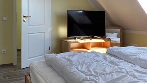 Une chambre à coucher avec un lit, un téléviseur posé sur un meuble en bois, une porte et une lucarne.
