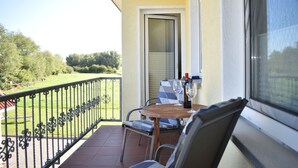 Un balcón con mesa y sillas, vista al jardín y puerta que da al interior.