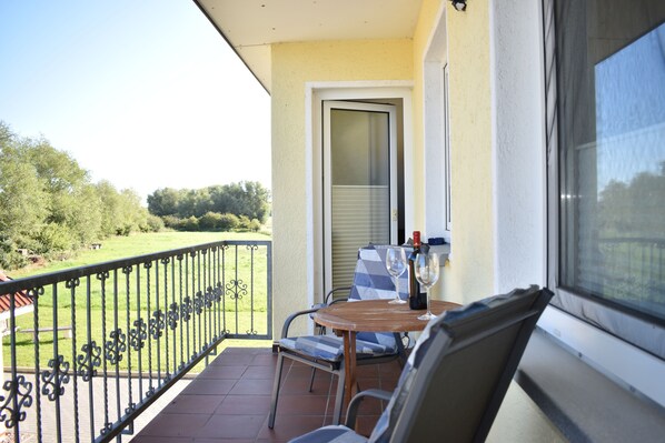 A balcony with a table and chairs, a view of the garden, and a door leading to the interior.