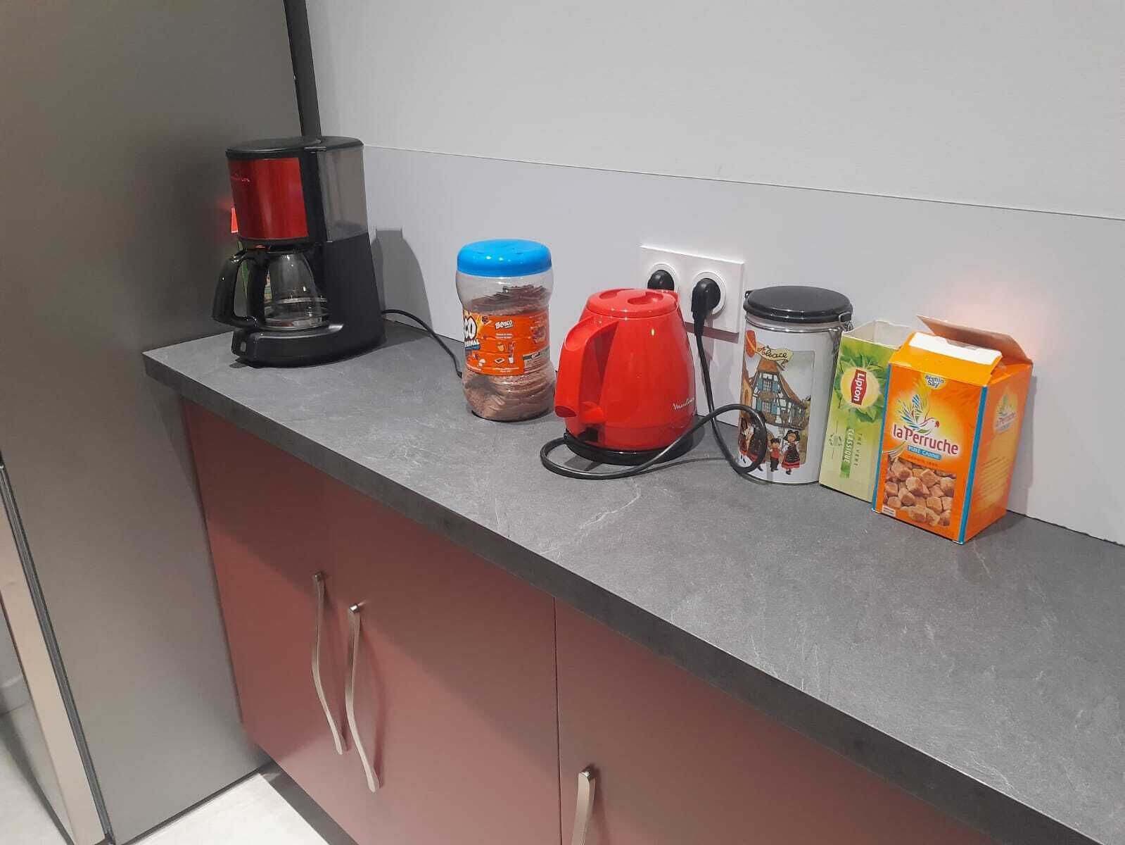 Una encimera de cocina con una cafetera, un hervidor rojo, un tarro de especias, un recipiente y un cartón de leche.