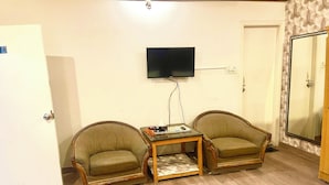Ein Zimmer mit zwei Sesseln, einem kleinen Tisch, einem an der Wand befestigten Fernseher und einer Tür.