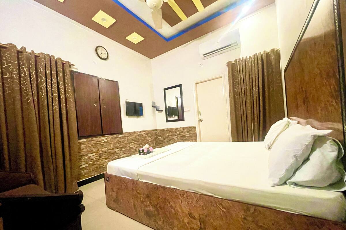 A hotel room with a bed, curtains, a clock, a television, and a wardrobe.
