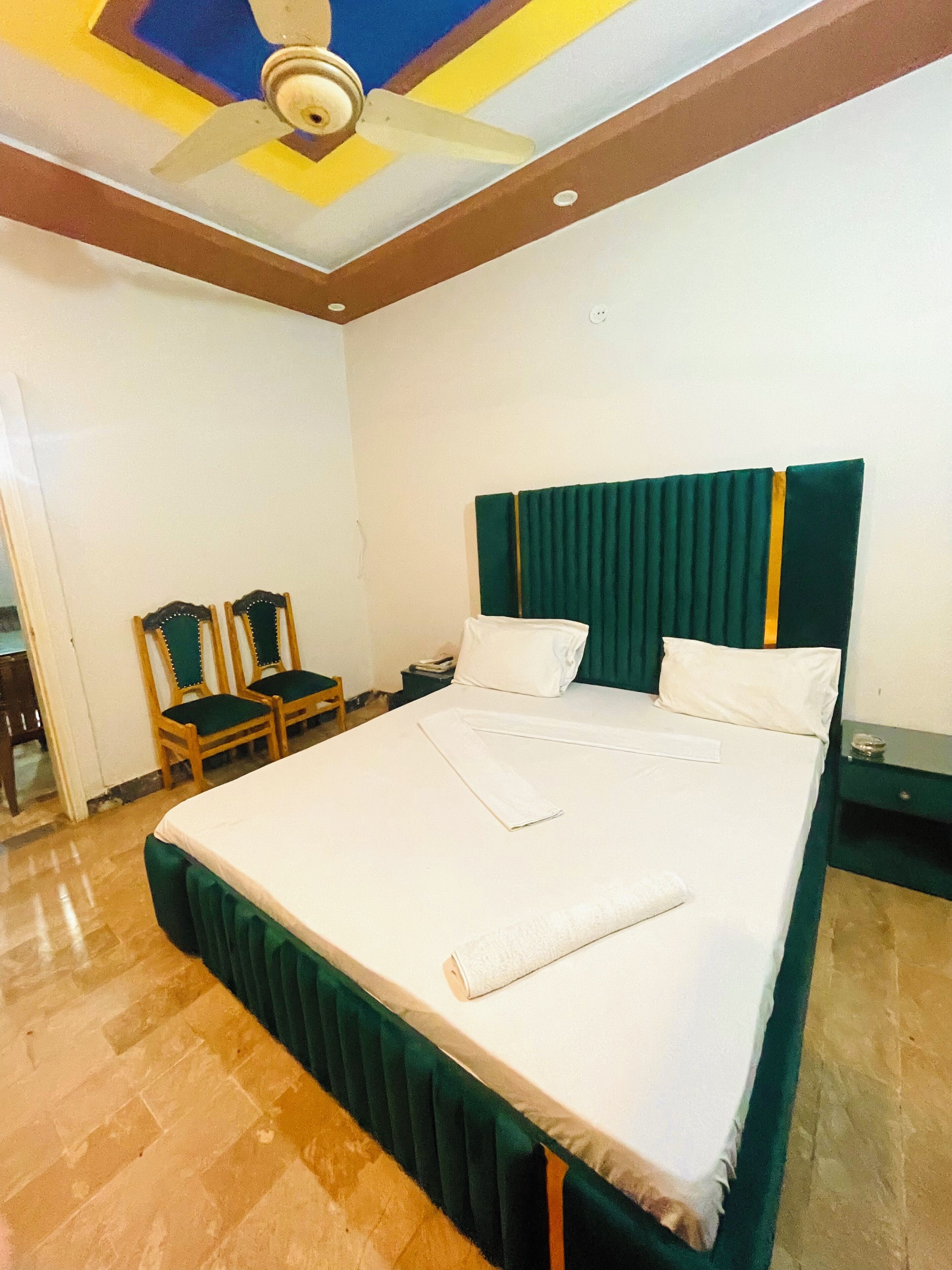 A hotel room with a large bed, two chairs, a nightstand, and a ceiling fan.
