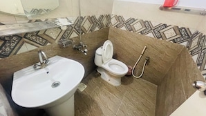 Ein Badezimmer mit Waschbecken, Toilette und Dusche. Der Boden ist mit gemusterten Fliesen ausgelegt, und an der Wand hängt ein Spiegel.