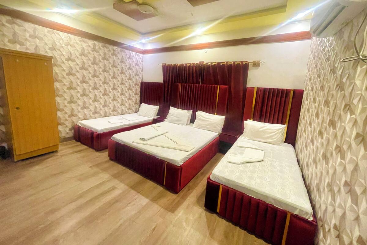 A hotel room with two beds, wooden flooring, patterned wallpaper, a ceiling fan, and a wooden wardrobe.