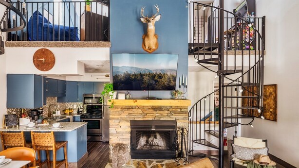 Un loft moderno con chimenea de piedra, una cabeza de ciervo decorativa, un televisor grande y una escalera de caracol.