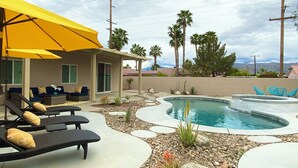 A pool area with lounge chairs and a yellow umbrella, surrounded by palm trees and a view of mountains. - Desert Poolside Haven (Cathedral City)