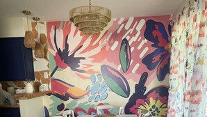 Et spiseområde med et hvidt bord, stole og et farverigt blomstermotiv på væggen.