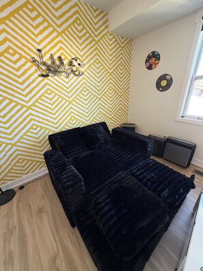 Ein Zimmer mit einer Wand mit Muster, einem schwarzen Sofa, einem Heizkörper und einem Fenster mit Jalousien.