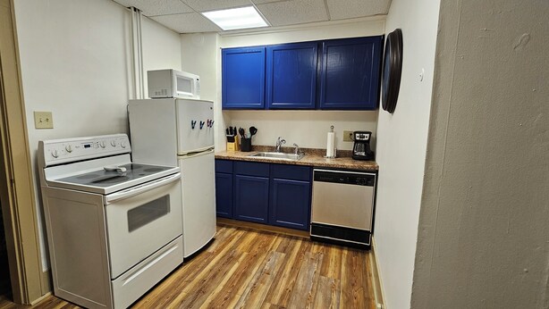 Une cuisine de taille réduite avec des appareils électroménagers blancs, des armoires bleues et un plancher en bois.