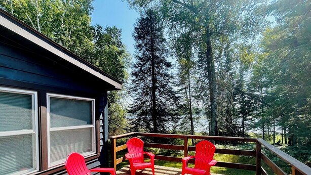 A wooden deck with four red chairs and a table, overlooking a forested area. - Jack The Horse Lake Cabin -Pool Table-Wifi-Tub-Trails-Peaceful-Dining Closeby! (Marcell)