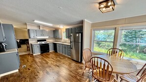 A modern kitchen with grey cabinets, a stainless steel refrigerator, and a dining area with a wooden table and chairs. - Jack The Horse Lake Cabin -Pool Table-Wifi-Tub-Trails-Peaceful-Dining Closeby! (Marcell)