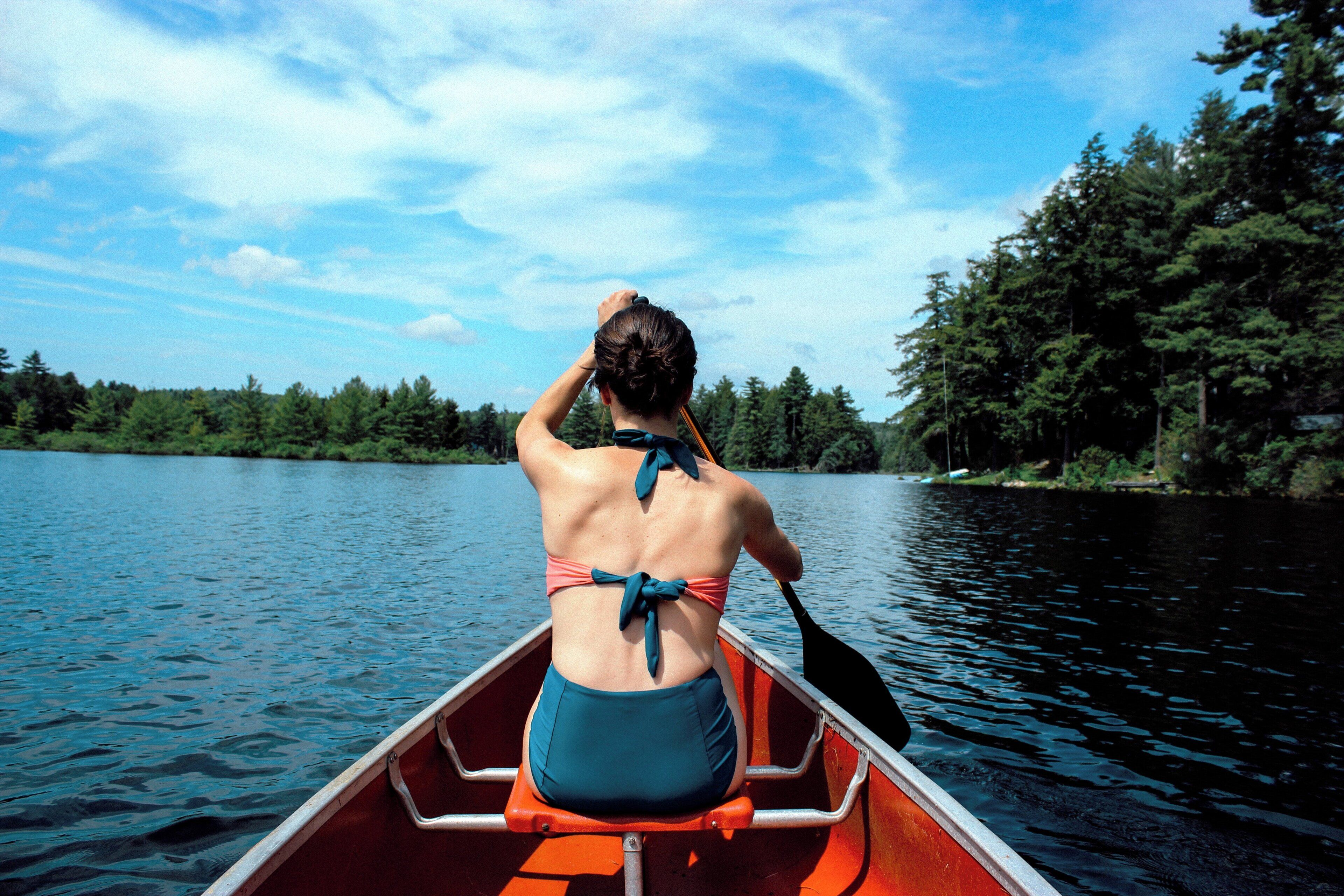 A person in a canoe on a calm lake with trees in the background.