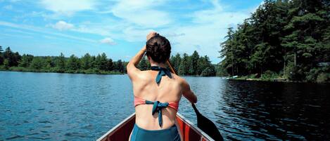 A person in a canoe on a calm lake with trees in the background.