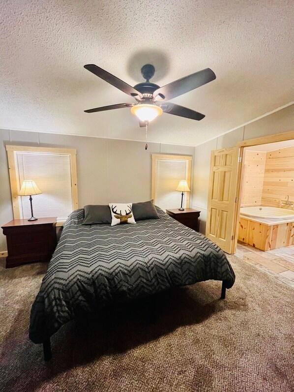 A bedroom with a bed, two nightstands, a ceiling fan, and a wooden door leading to a bathroom.