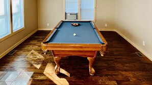 A pool table in a room with wooden flooring, two windows with blinds, and a ceiling light fixture. - Jack The Horse Lake Cabin -Pool Table-Wifi-Tub-Trails-Peaceful-Dining Closeby! (Marcell)