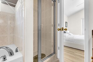 A modern bathroom with a glass shower door, a white sink, and a bed visible through the door. - Disney Area 4BR Home with Heated Private Pool (Kissimmee)
