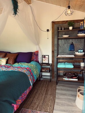Ein Schlafzimmer mit Bett, Nachttischen, einem Regal mit Pflegeprodukten und einer Hängelampe.