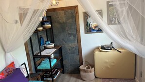 Een knus slaapkamer met een hemelbed, een klein houten plankje met toiletartikelen, een koffer en een lijst met een foto aan de muur.