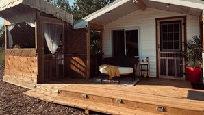Een houten chalet met een overdekte veranda, een schuifdeur en een klein zitgedeelte met een bank en een tafel.