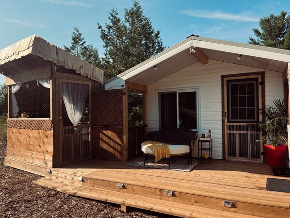 Eine Holzhütte mit einer überdachten Veranda, einer Glastür und einer kleinen Sitzecke mit einer Bank und einem Tisch.