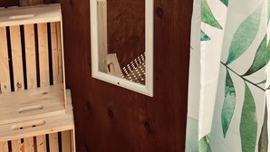 Een houten hutje met een spiegel aan de wand, een houten bank en een gordijn met een bladpatroon.