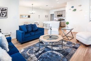 Een moderne woonkamer met een blauwe bank, een glazen salontafel en een witte fauteuil.