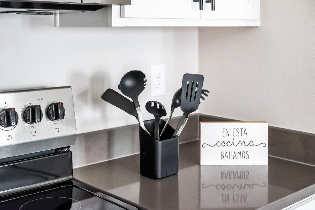 A kitchen with a stove, a black utensil holder, and a sign that reads 'EN ESTA cocina bailamos'.
