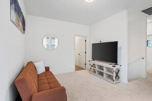 Een woonkamer met een bank, een televisie op een dressoir, een deur naar een andere kamer en een ronde spiegel aan de muur.