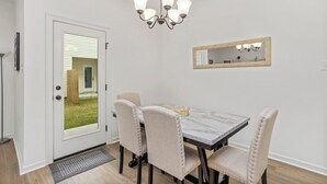 Un comedor con una mesa de mármol, cuatro sillas tapizadas, una lámpara de araña, un espejo y una puerta que da al exterior.