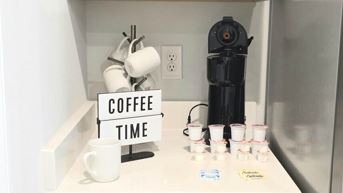 Una postazione caffè con un cartello, una macchina da caffè, tazze e bustine di zucchero.