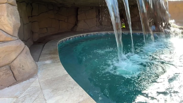 Een zwembad met een waterval, omringd door stenen muren.