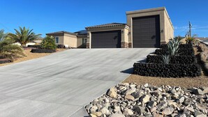 Een woonhuis met een verharde oprit, twee garage deuren, en een aangelegde voortuin met stenen en beplanting.