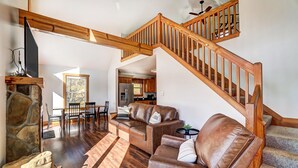 A spacious living area with a wooden staircase, leather sofas, and a stone fireplace. - Lakefront Home: Fishing + Kayaking + King Bed + Hot Tub (Logan)