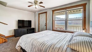 A bedroom with a bed, a TV, a ceiling fan, and a large window with a view. - Lakefront Home: Fishing + Kayaking + King Bed + Hot Tub (Logan)