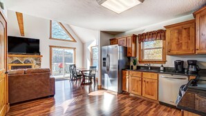 A spacious kitchen with wooden cabinets, a stainless steel refrigerator, and a dining area with a table and chairs. - Lakefront Home: Fishing + Kayaking + King Bed + Hot Tub (Logan)