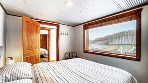 Un dormitorio con una cama grande, una puerta de madera, una ventana con vistas a un paisaje nevado y una mesita con una silla.