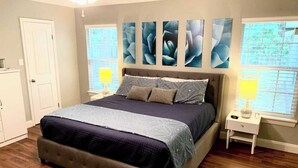 Quarto com uma cama grande, mesa de cabeceira, penteadeira e janela com persianas.