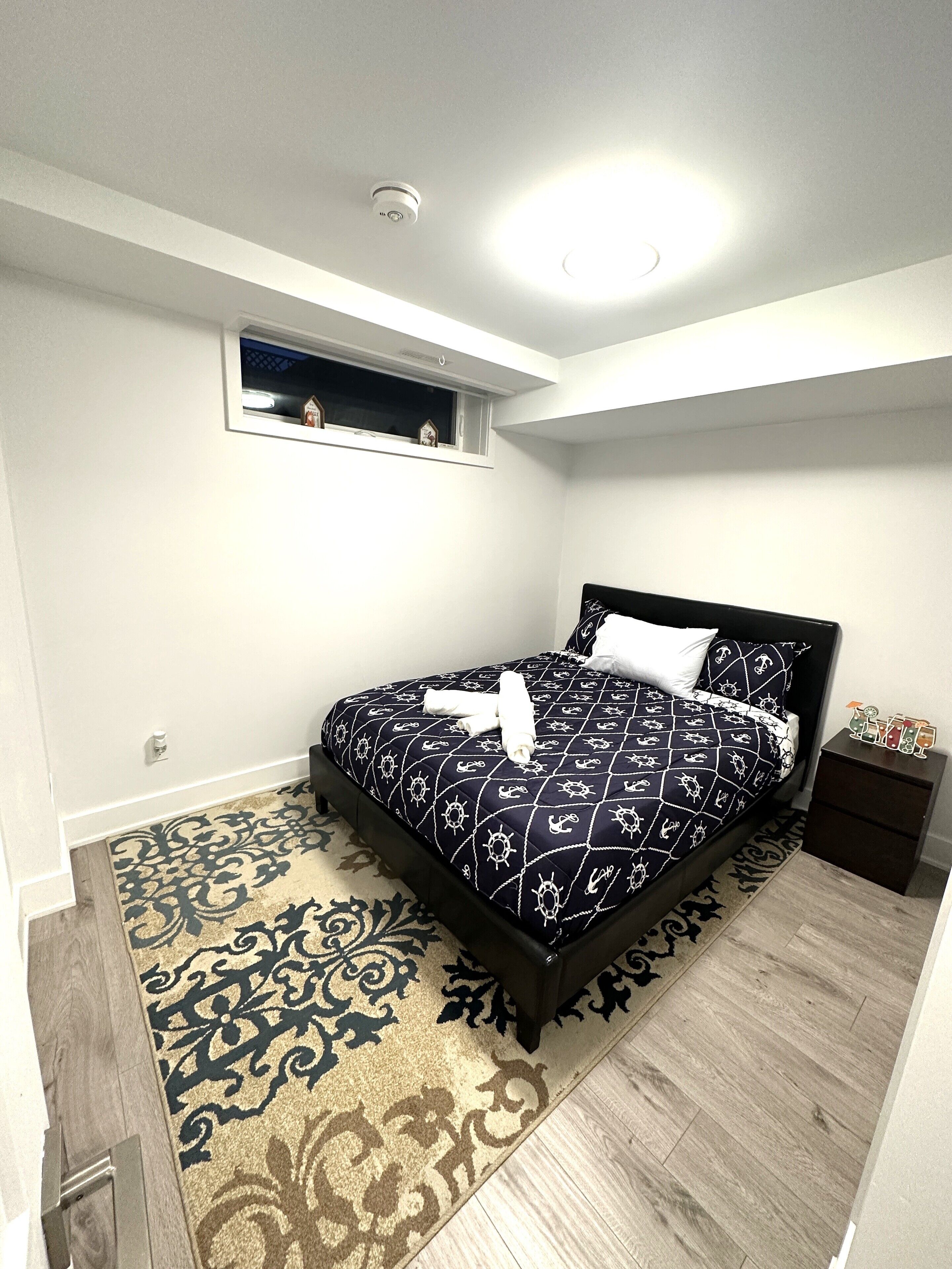 Un dormitorio con cama, mesita de noche, ventana y luz en el techo.