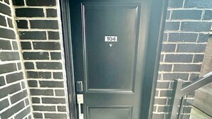 A dark-colored door with a number plate '104' and a welcome mat with floral designs. - Cozy 2-Bedroom Condo with Parking in Niagara Falls (Niagara Falls)