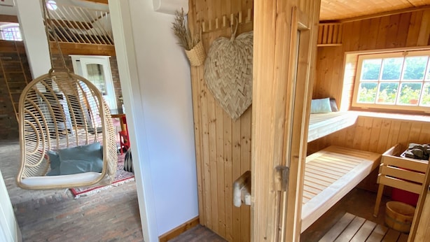 A wooden cabin interior with a hanging chair, a woven rug, and a bed with a window view.
