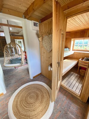 A wooden cabin interior with a hanging chair, a woven rug, and a bed with a window view. - Tobacco Barn (Kalkar)