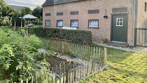 A brick building with a green door, multiple windows, and a garden area with a wooden fence and plants.
