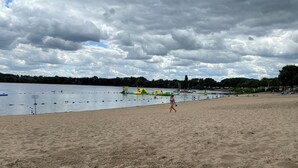 A sandy beach with a calm lake, boats, and a playground.