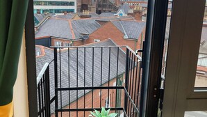 Un balcone con ringhiera in metallo, una pianta in vaso e vista su un paesaggio urbano con edifici e una gru.